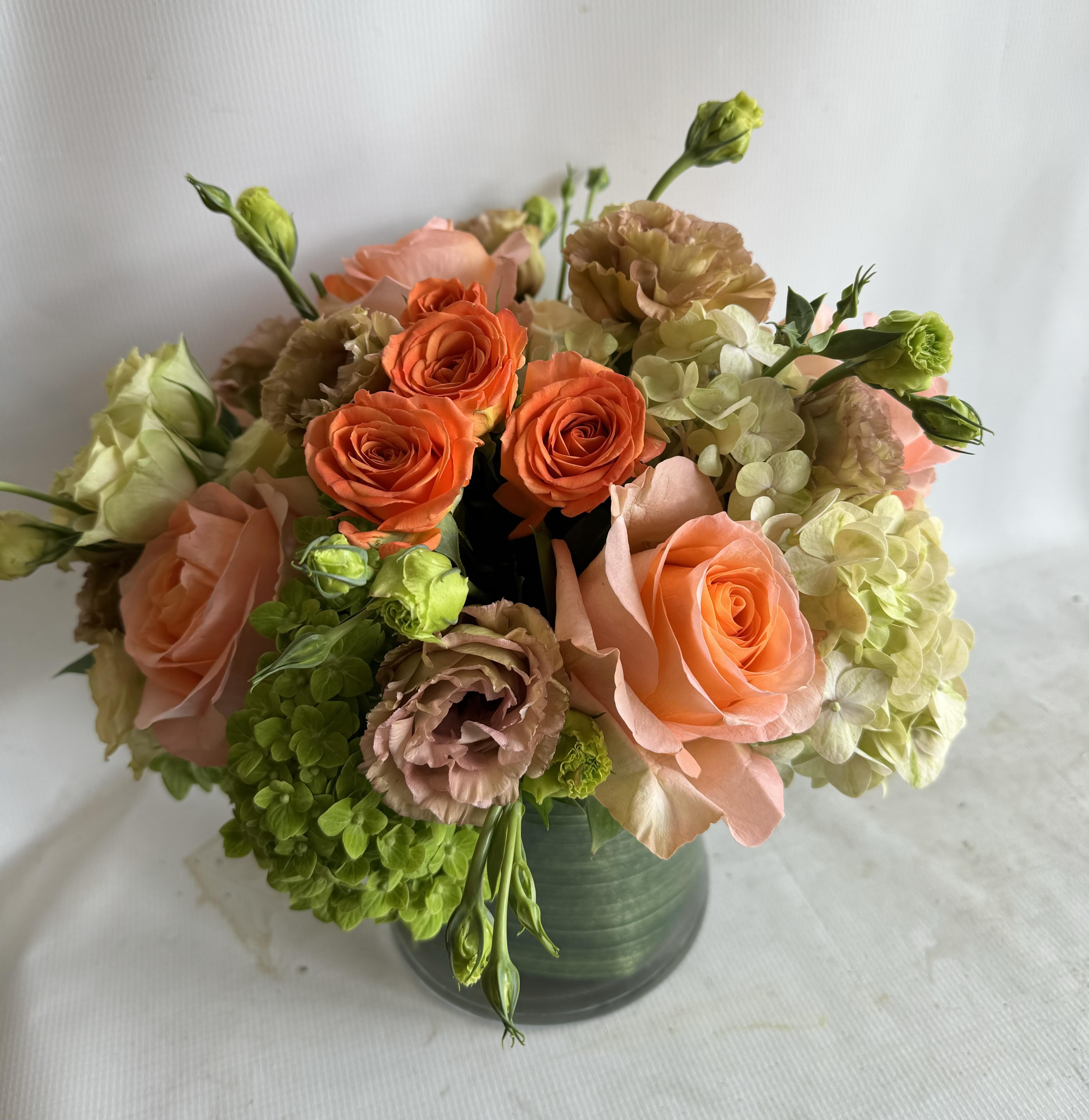 Bouquet of orange and peach roses with green hydrangeas in a dark vase