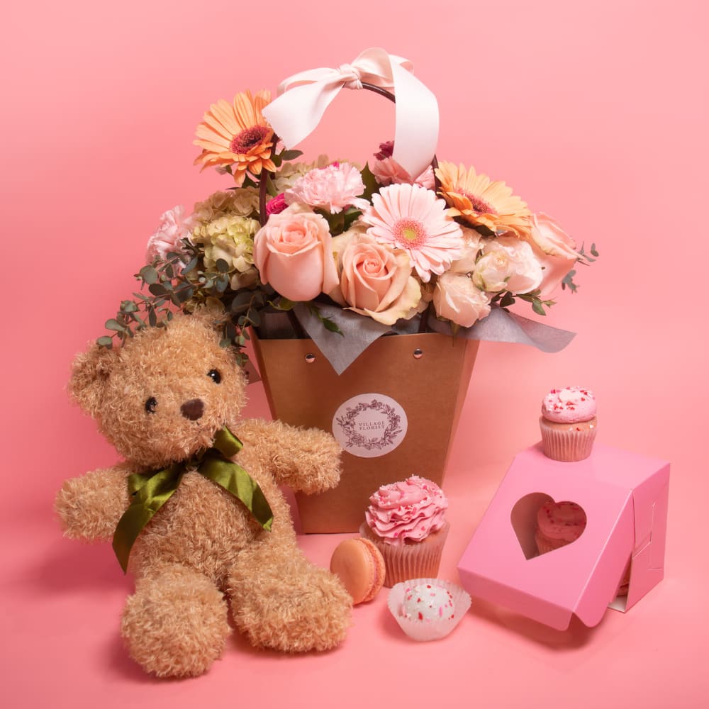 Flower basket with roses and gerberas, plus a teddy bear and cupcakes on a pink background