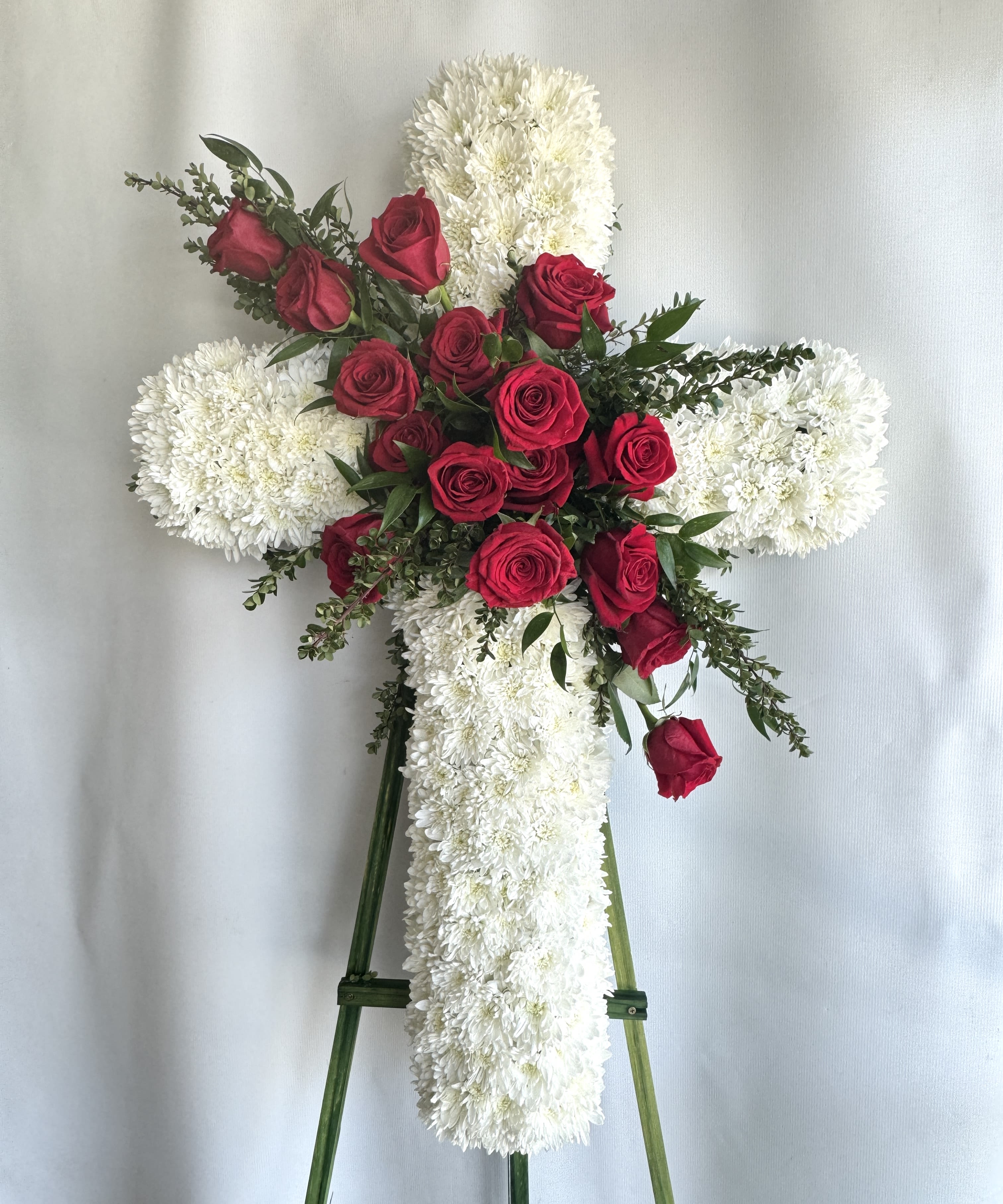 Heartfelt Cross - This peaceful cross is not only a beautiful tribute, but a symbol of hope and faith during times of loss. It is lovingly created with fluffy white cushion mums and a striking red rose cluster, making it a fitting and respectful expression of sympathy. Available in three sizes - 30 inches, 36 inches, and 45 inches - this cross will bring comfort and solace to those in mourning. Each cross is hand-designed with care and can be customized in your preferred color palette. Easel stand included for display at the service.