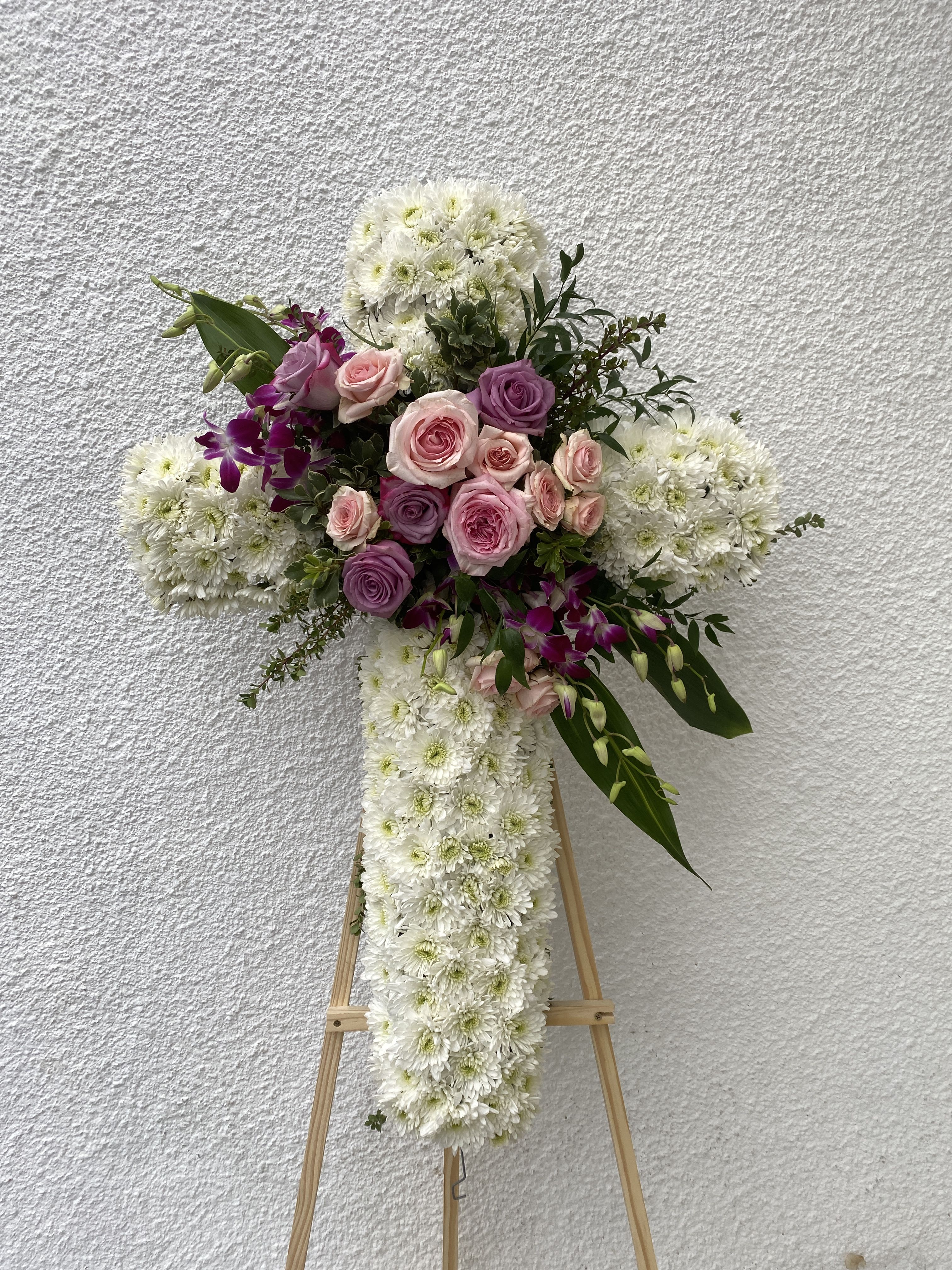 White floral cross on an easel with pink and purple roses