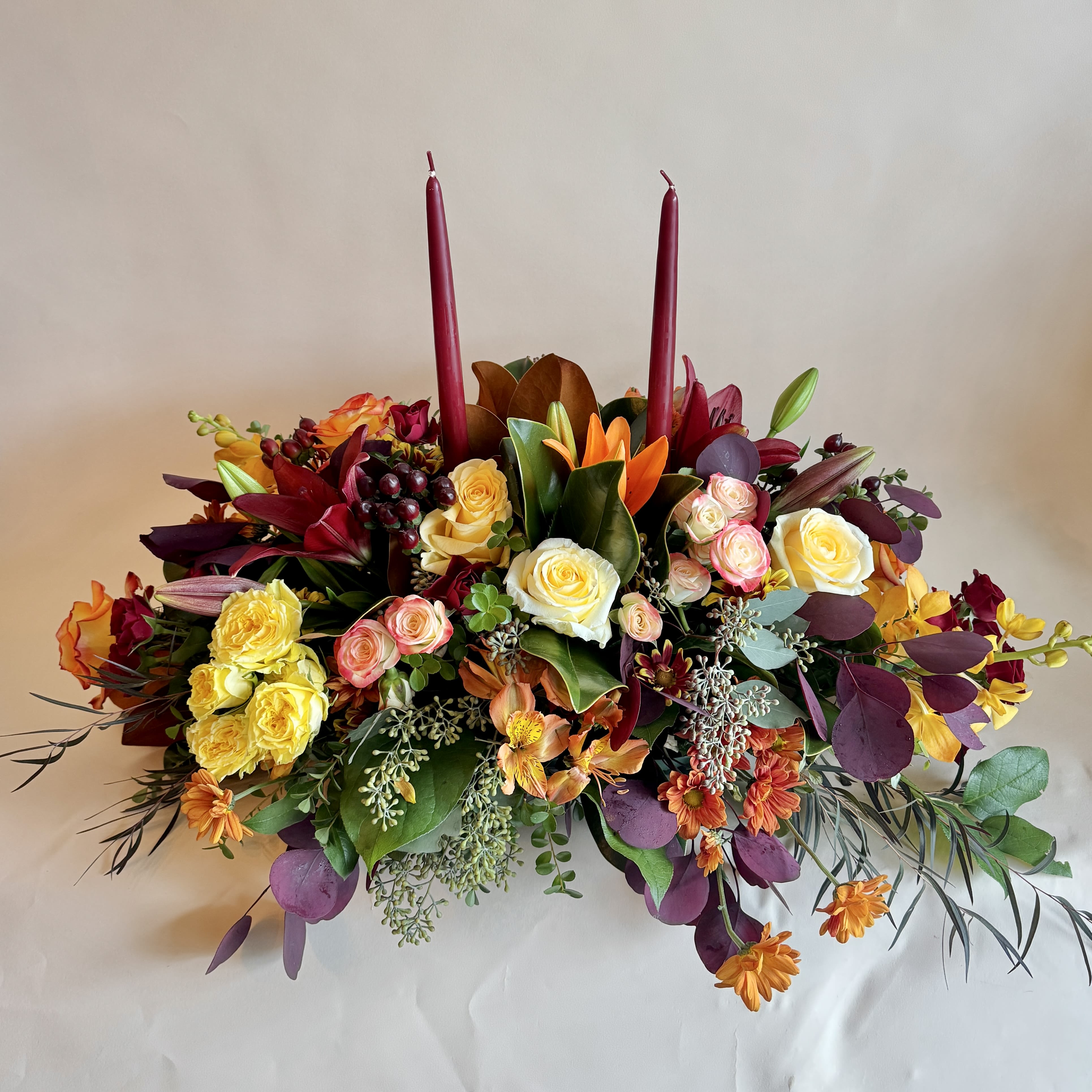 Thanksgiving Centerpiece - This centerpiece is long and short, perfect for any dinner table, with orange and yellow roses, seeded eucalyptus, wheat, cattails, greens, and tea leaves.