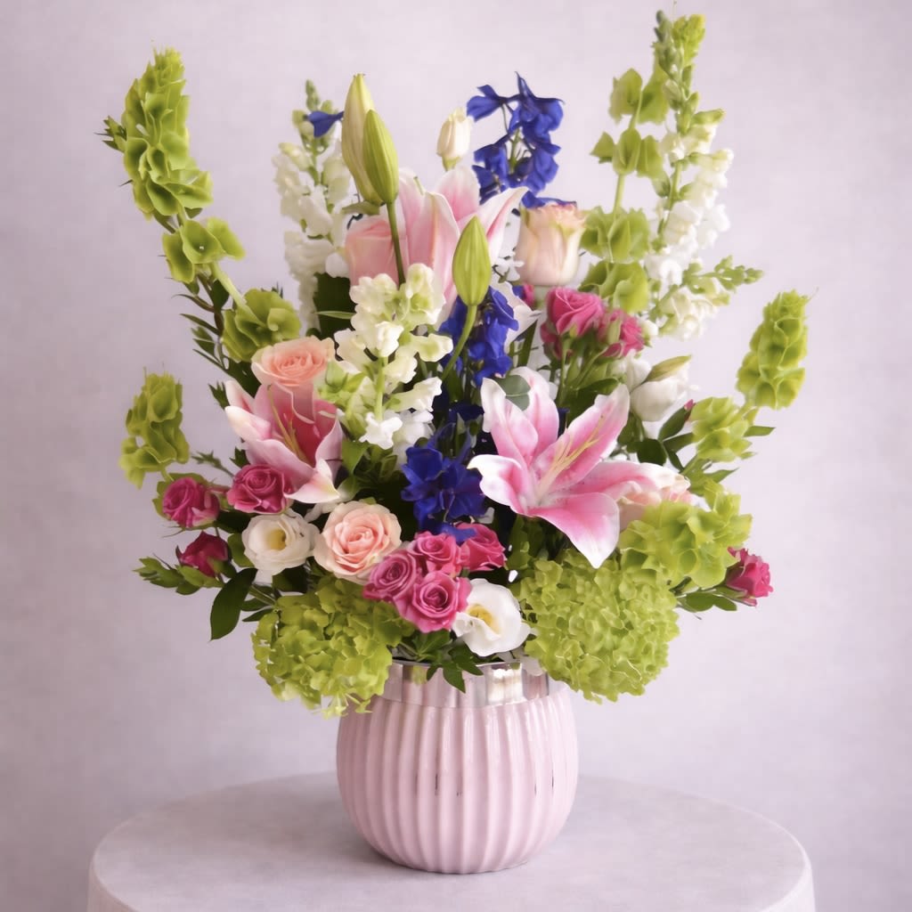 Easy Elegance - Tall draping arrangement filled with roses, hydrangeas, lilies, and bells of Ireland. In beautiful pastel colors. 