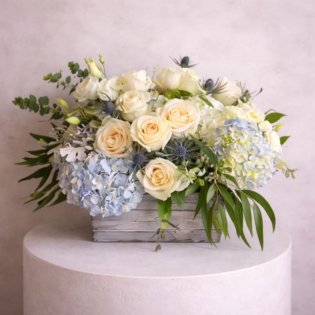 Cream roses and blue hydrangeas arranged in a rustic wooden box