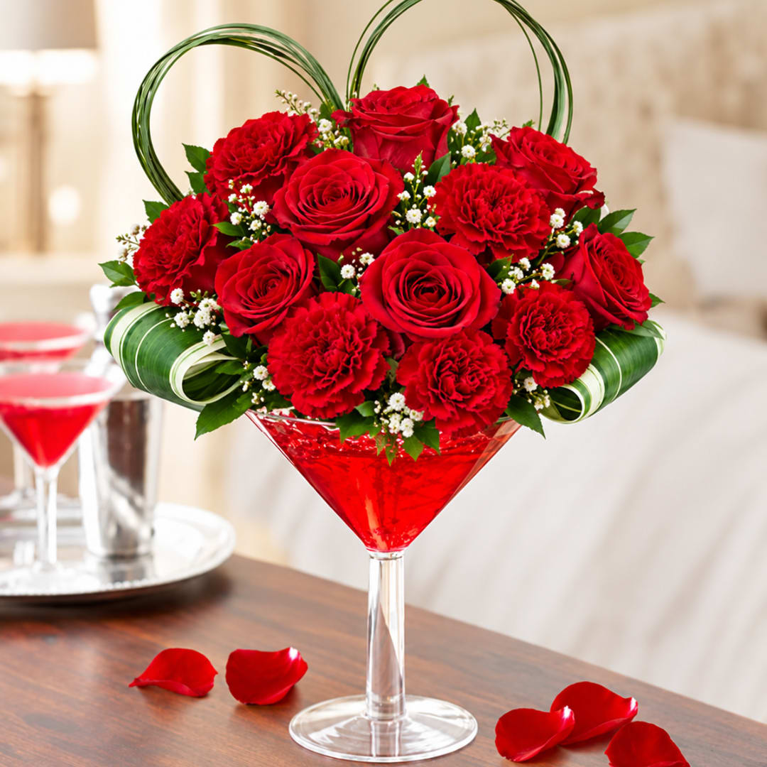 Red roses and carnations arranged in a martini glass with green ribbon loops