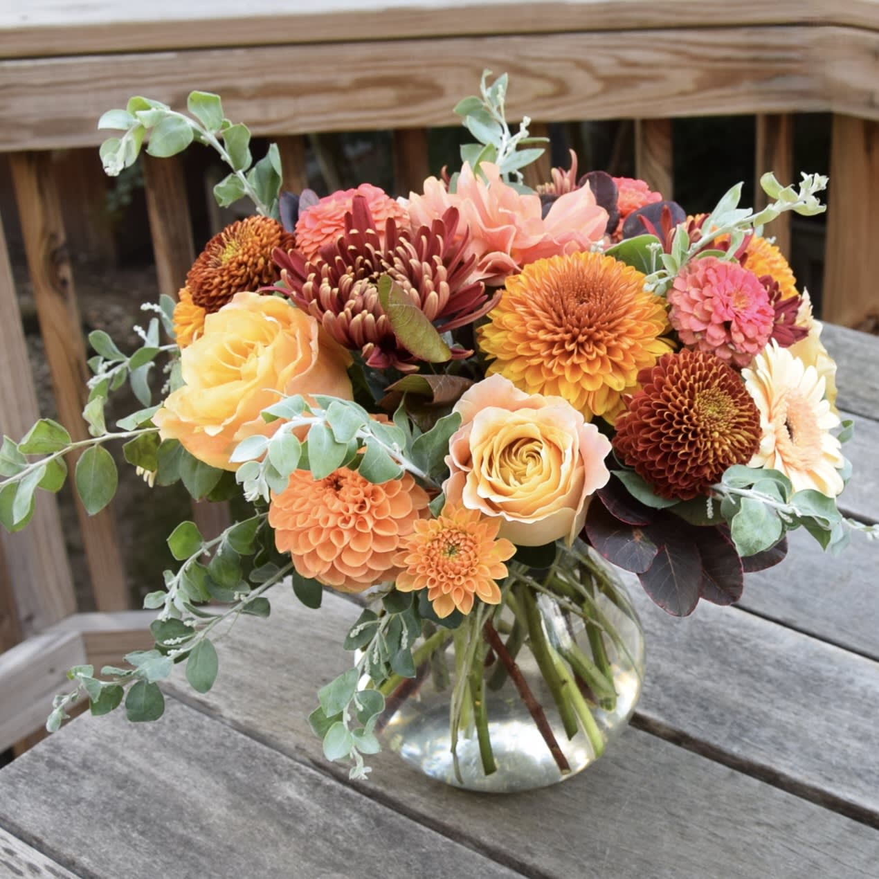 Apple Cider - Autumnal flower arrangement in a glass vase with beautiful seasonal flowers like cremons, gerber daisies, dahlias and more. Colors may vary, usually a mix of yellows, oranges, peach and brown.  