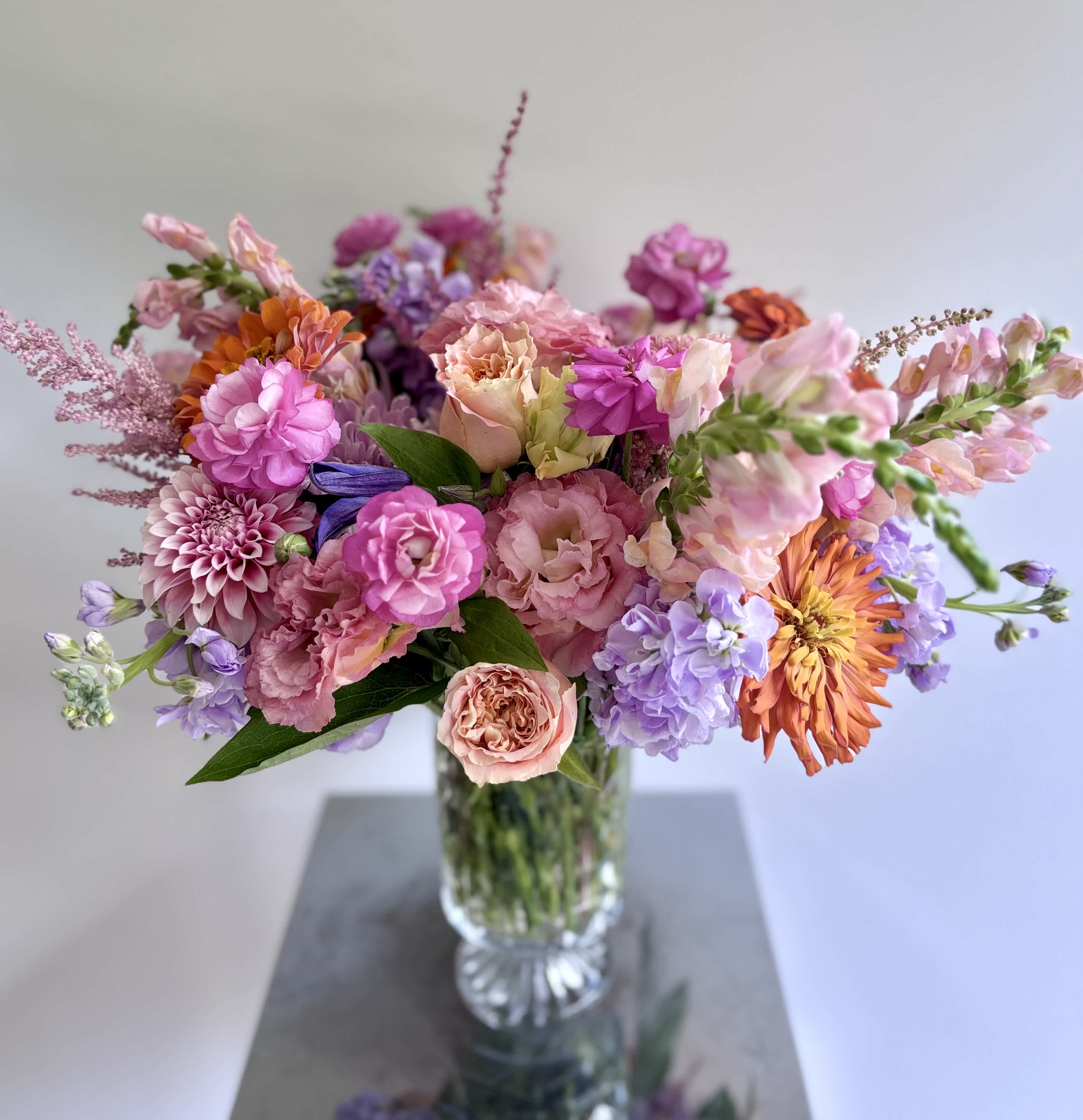 Mixed pink, peach, purple, and orange flowers in a clear glass vase