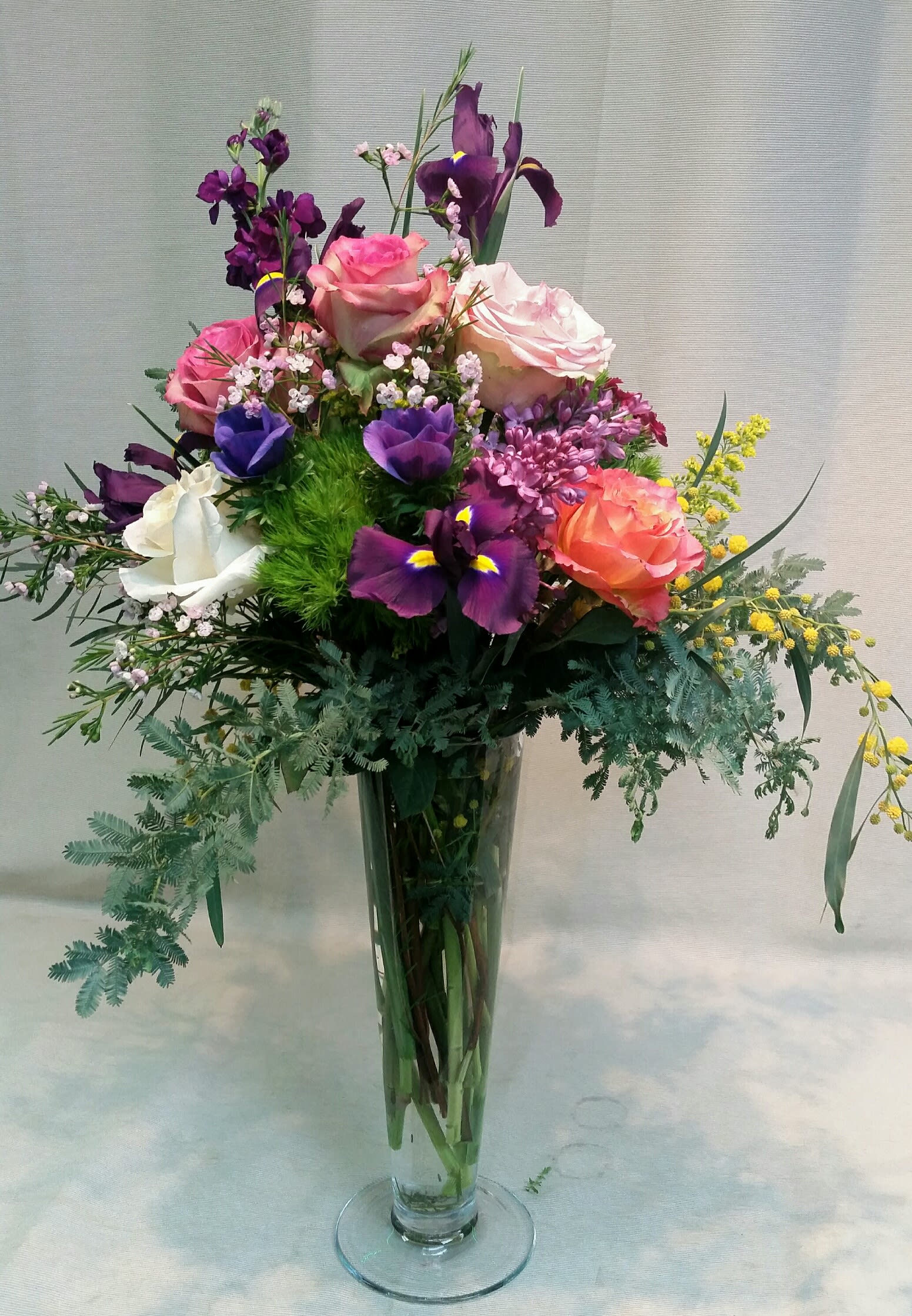 Tall mixed bouquet of roses and purple iris in a clear glass vase