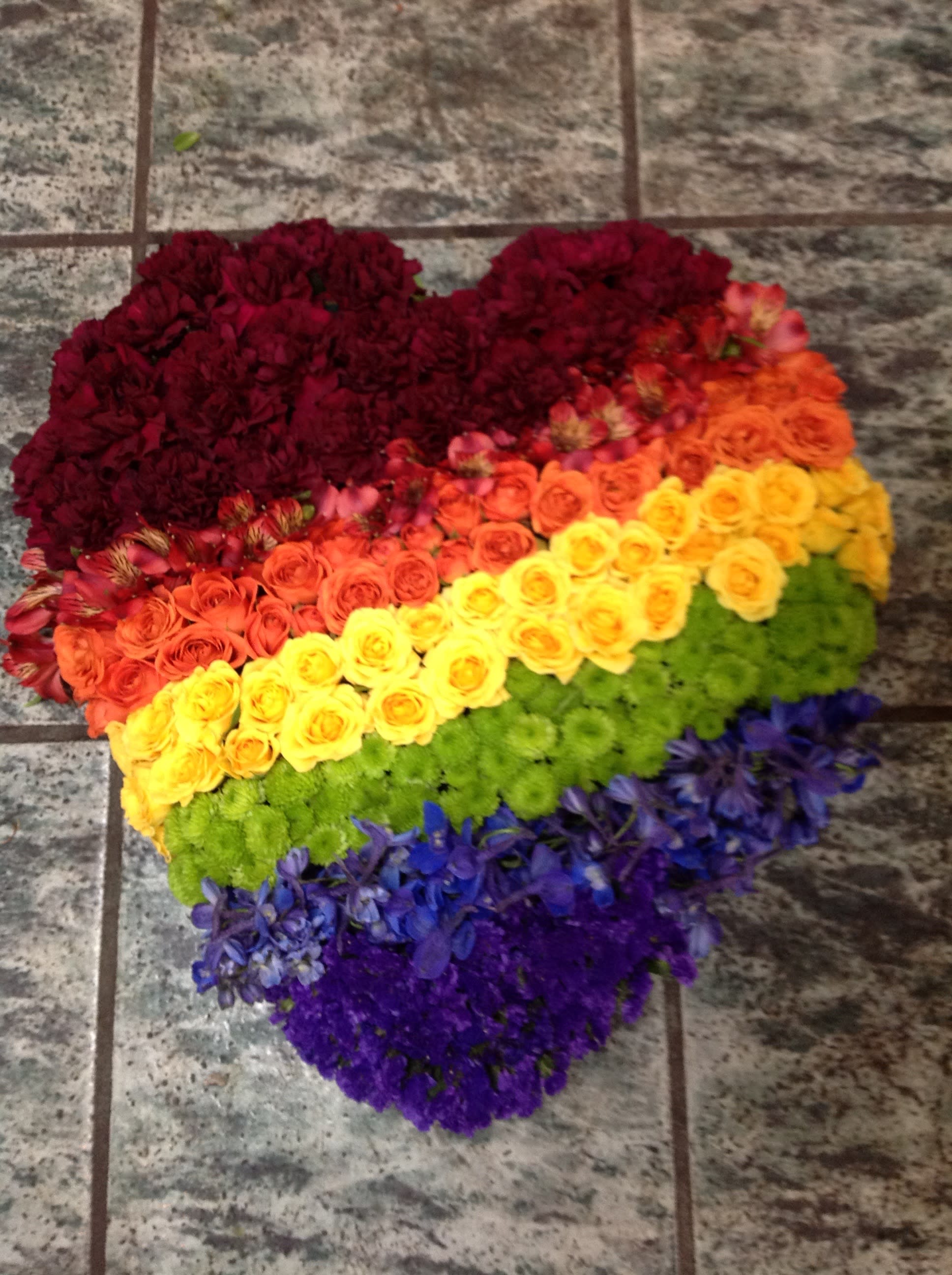 Heart-shaped floral arrangement in rainbow colors on a tiled floor