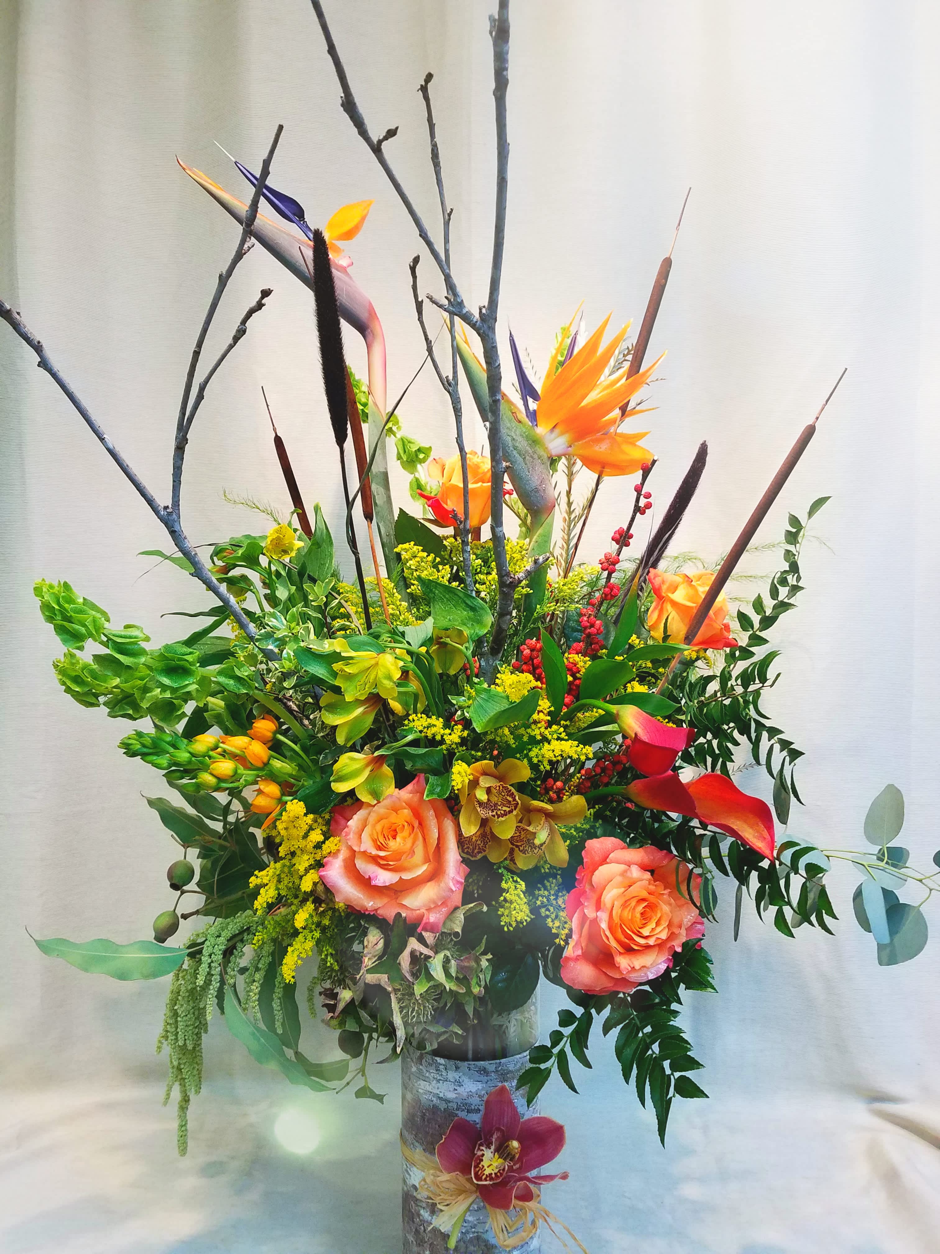Tall tropical floral arrangement with orange roses and bird of paradise in a vase