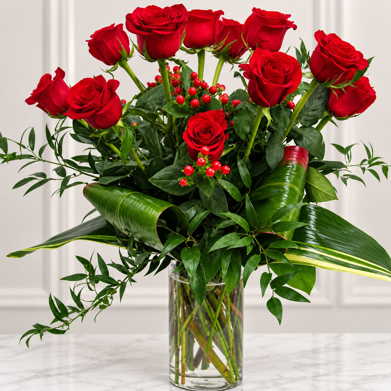 Red roses arranged in a clear glass vase with glossy greenery