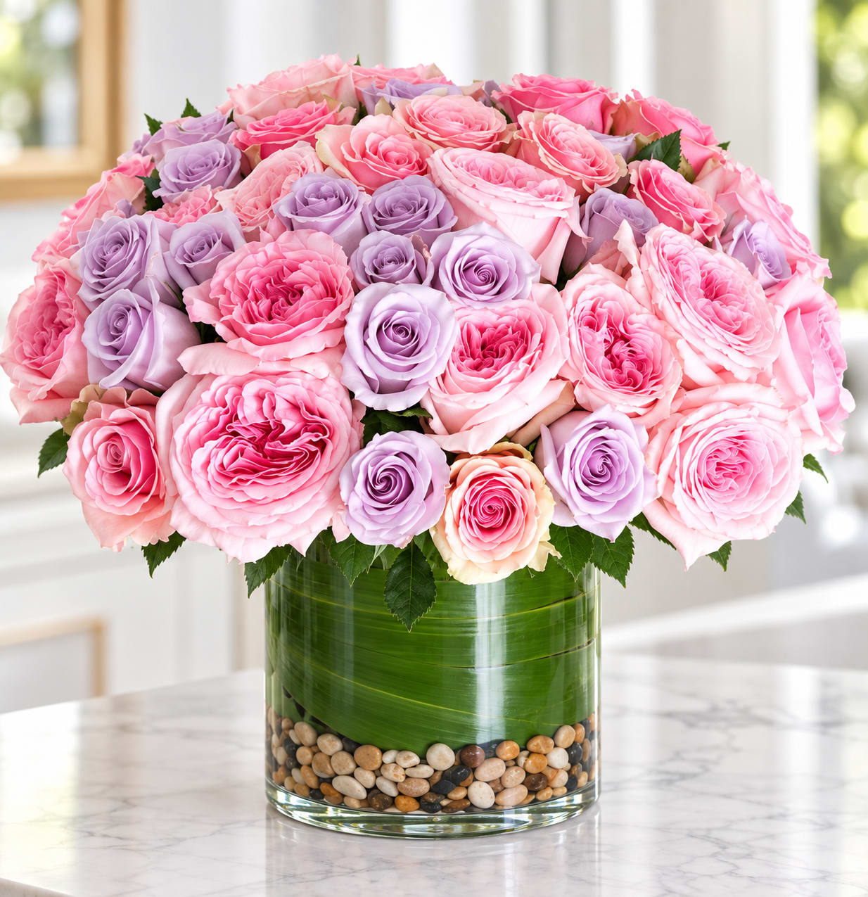 Pink and lavender roses arranged in a clear glass vase with pebbles