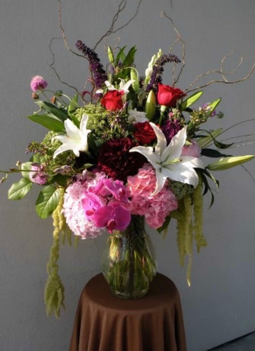 Tall mixed bouquet in a glass vase with red roses, white lilies, and pink blooms