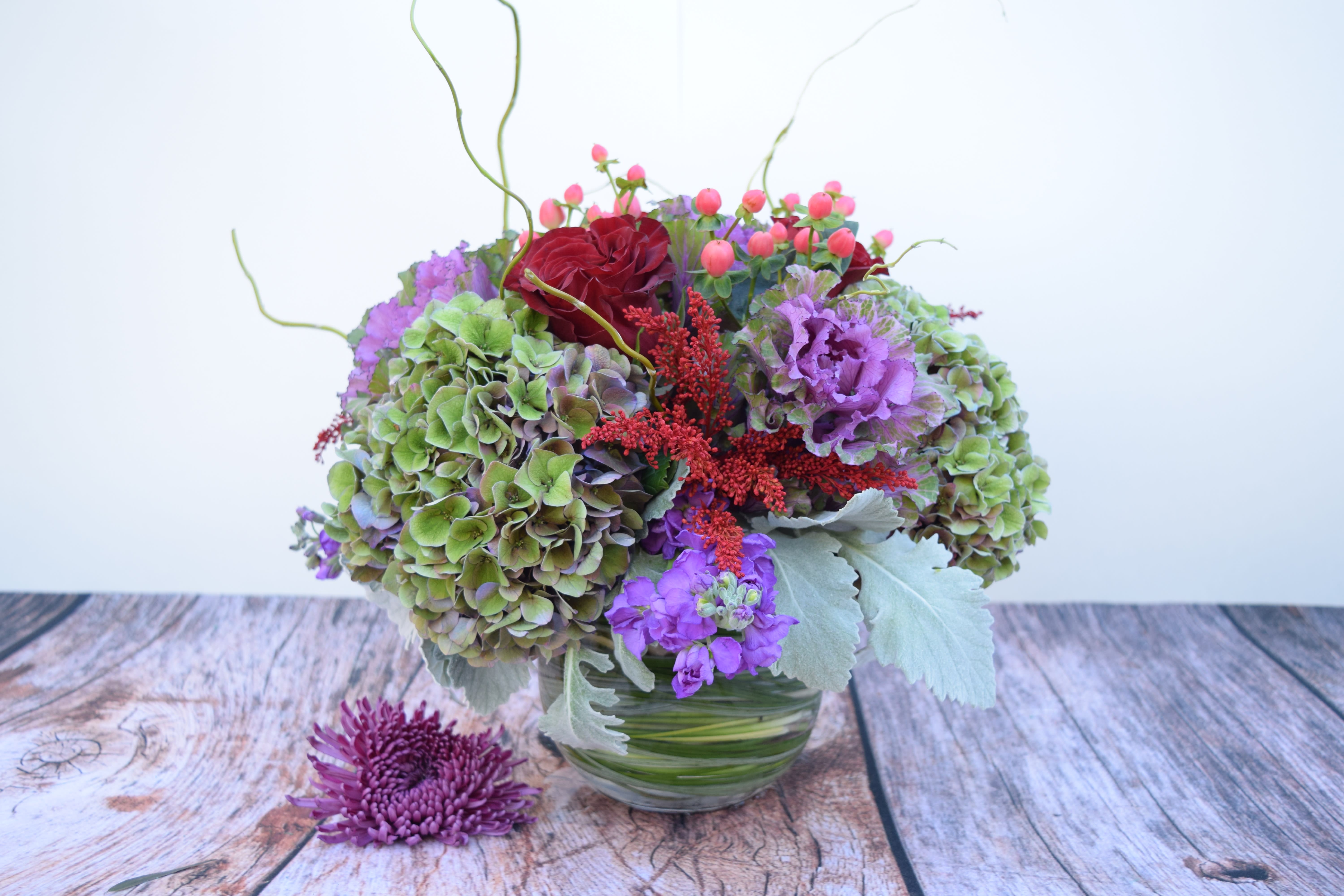 Mixed bouquet with hydrangeas, roses, and purple blooms in a glass vase