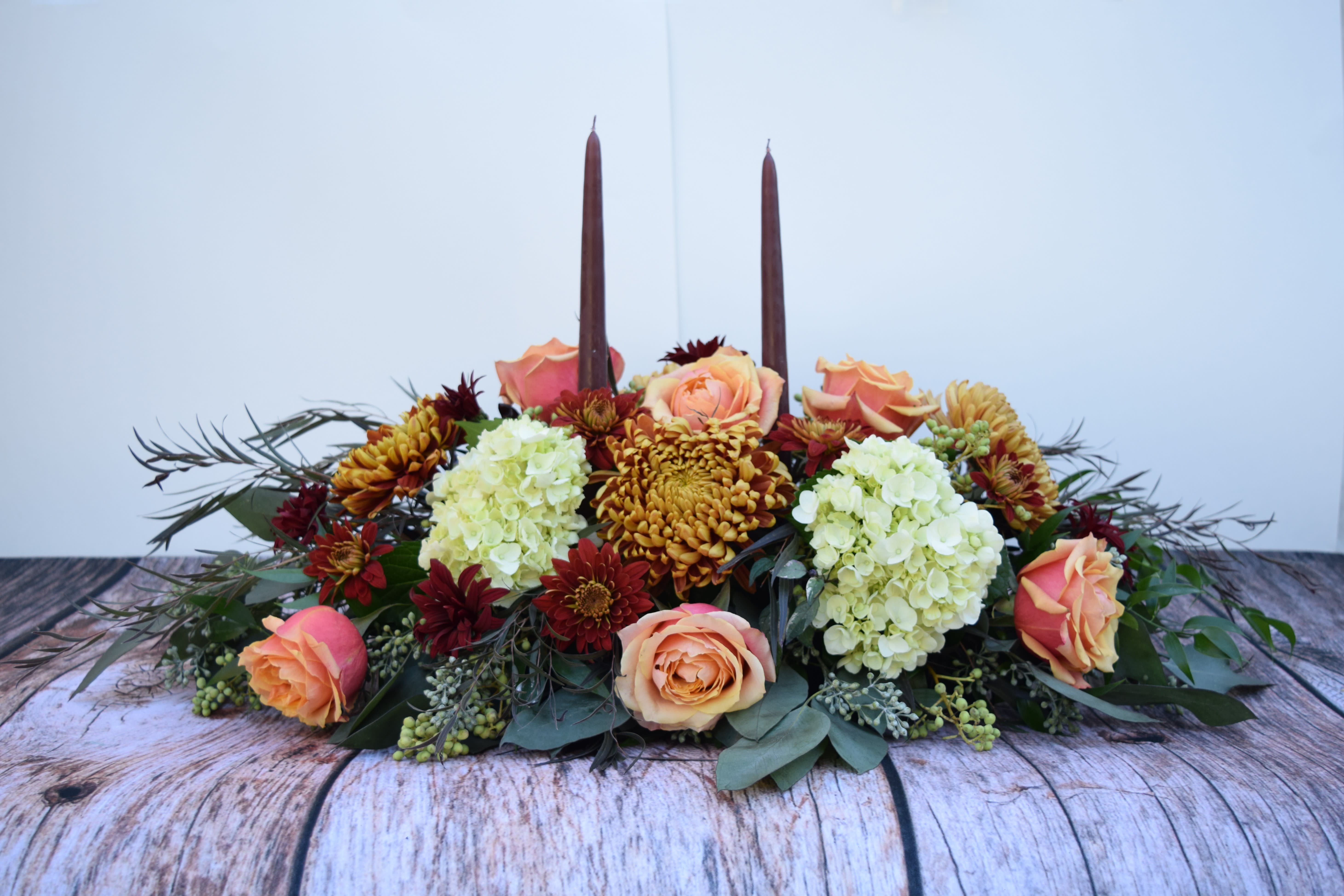 Low floral centerpiece with peach roses, white hydrangeas, and burgundy candles