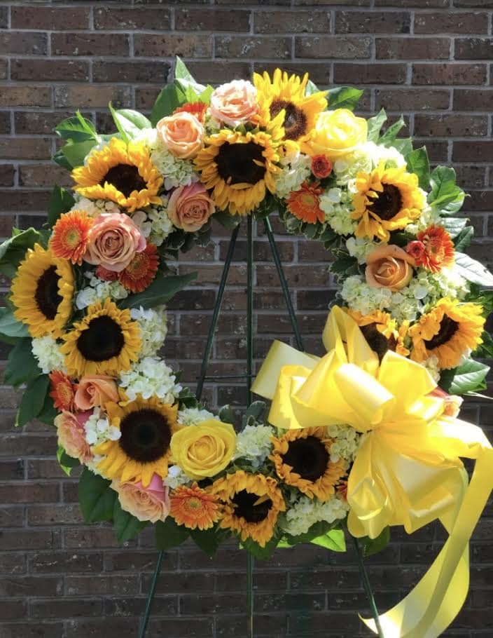 Standing wreath of sunflowers, roses, and other bright blooms with a large yellow bow on an easel