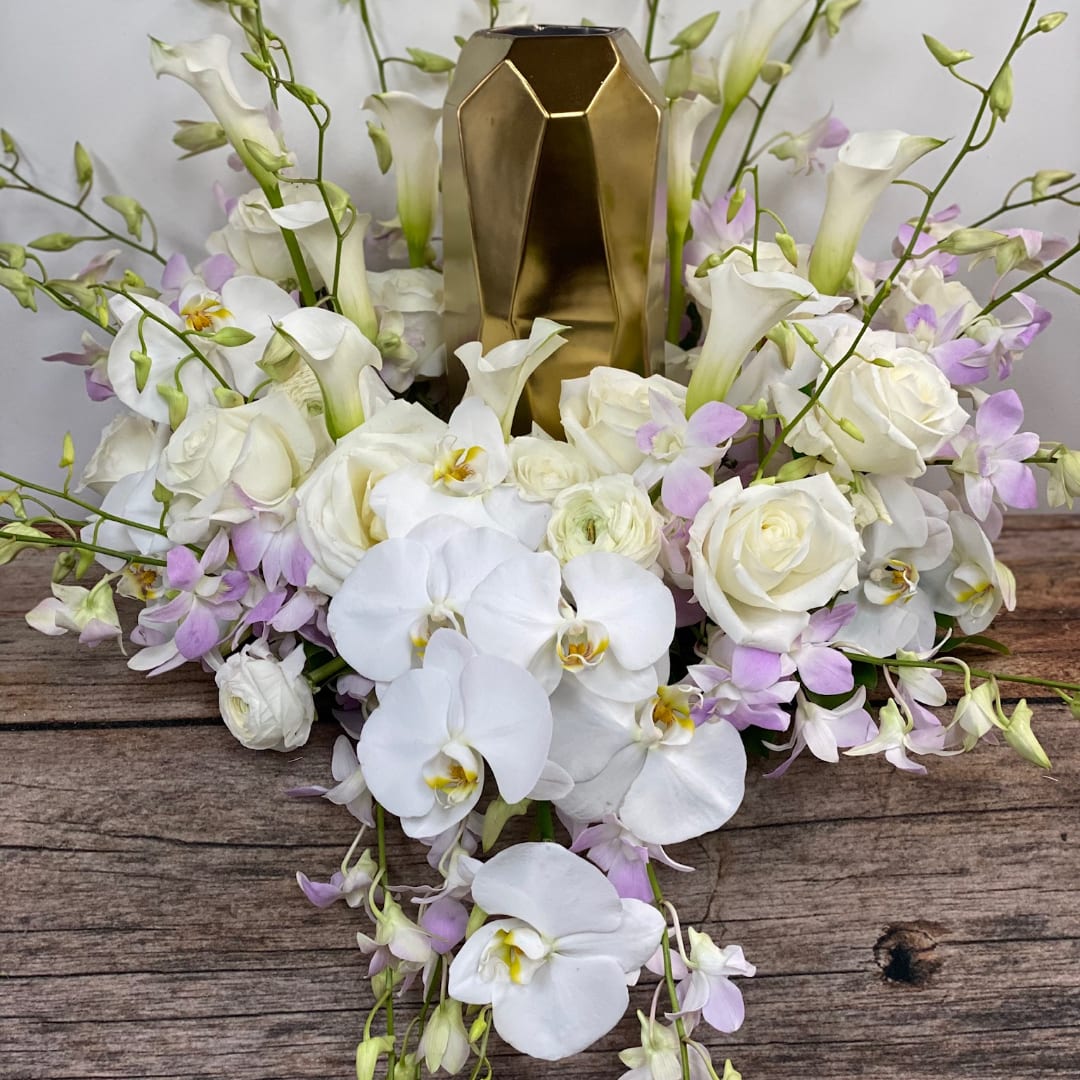 White orchids and roses arranged around a gold geometric vase