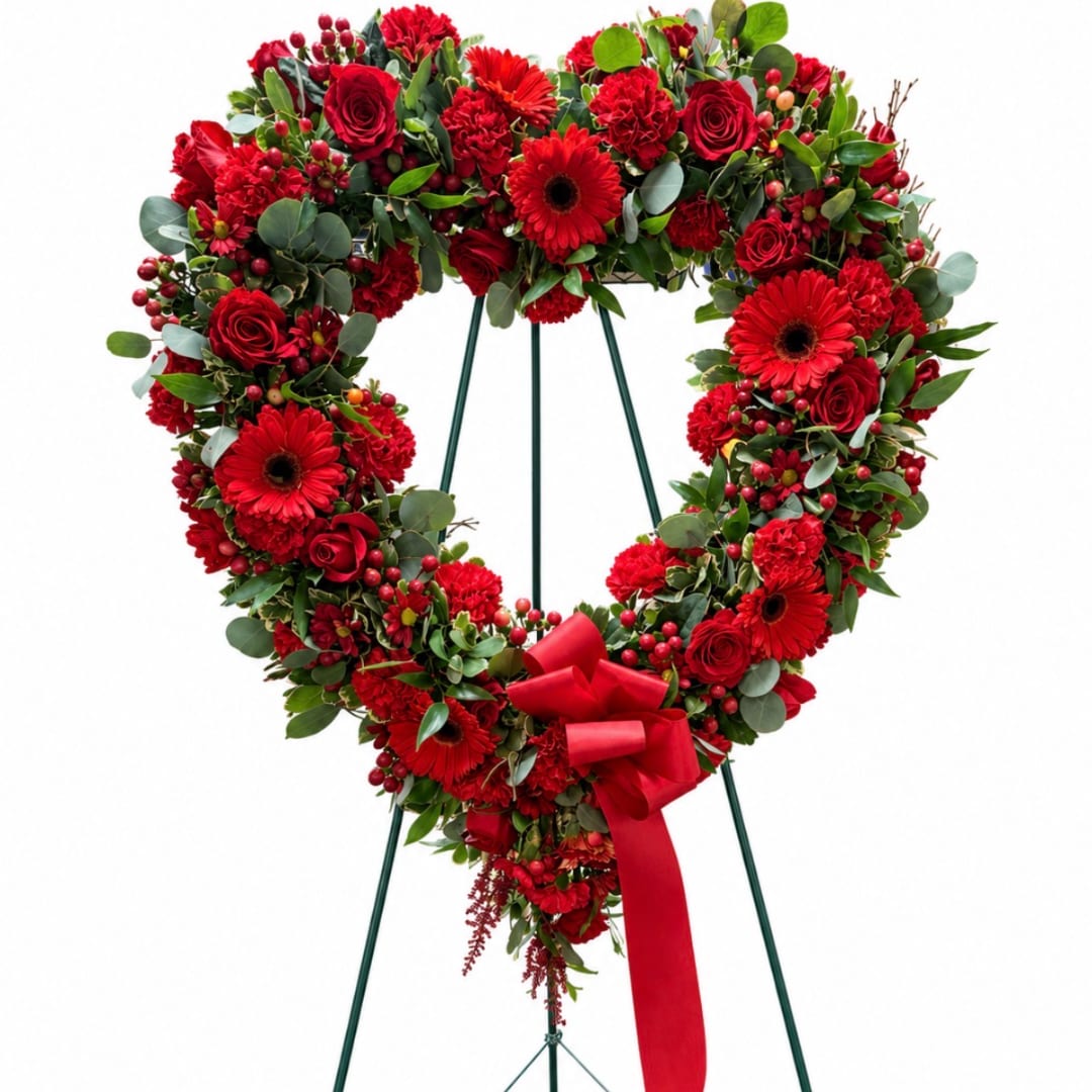 Heart-shaped red floral wreath on a stand with a red ribbon bow