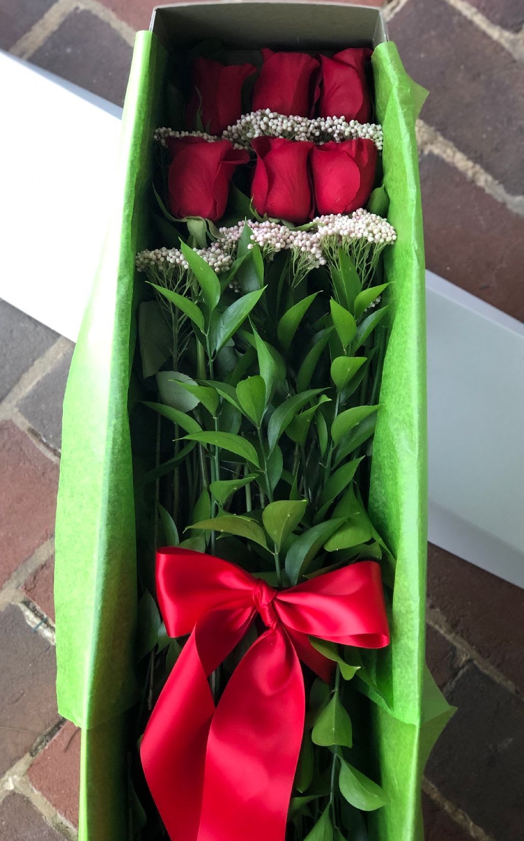 Boxed arrangement of long-stem red roses with a red satin bow in green tissue paper