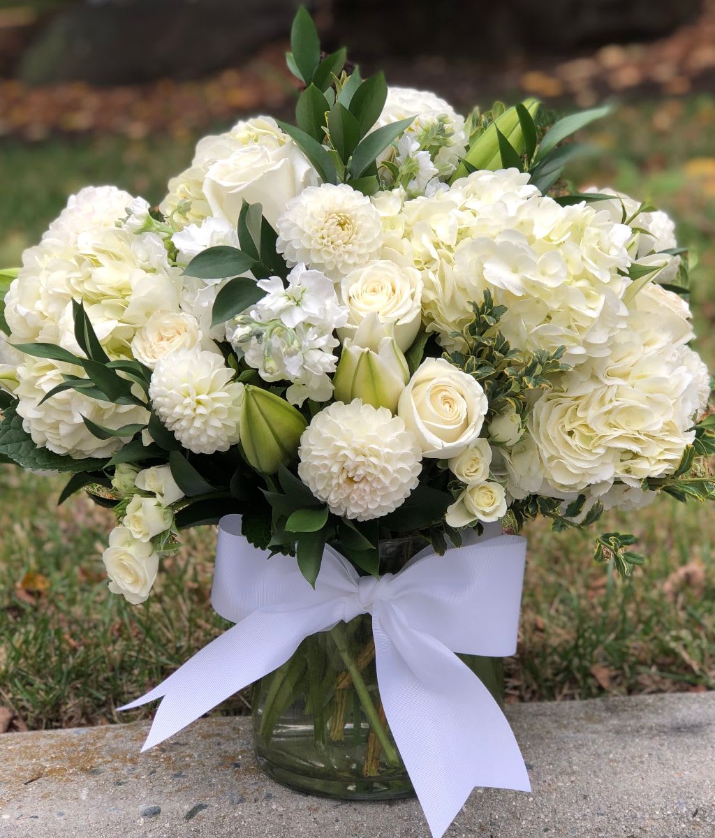 Peaceful Bliss - Peaceful Bliss | Wilmington, Delaware Florist  Experience serene elegance with our Peaceful Bliss arrangement, exclusively crafted by Petals Flowers and Fine Gifts — your trusted local florist in Wilmington, Delaware. This luxurious, all-white floral design features lush white hydrangea, classic white roses, elegant white dahlias, graceful white lilies, and fragrant white stock, all artfully arranged in a clear glass cylinder vase. The harmonious blend of fresh white blooms creates a sophisticated and calming centerpiece, perfect for any occasion.  Whether you’re sending sympathy flowers, celebrating a special milestone, or simply brightening someone’s day, Peaceful Bliss captures the essence of purity and timeless beauty.  As a boutique flower shop in Wilmington, Delaware, we specialize in premium, custom floral arrangements tailored to your needs. We proudly offer same-day, tax-free flower delivery throughout Wilmington, Hockessin, Newark, Glen Mills, Chadds Ford, Kennett Square, and surrounding areas — always backed by our satisfaction guarantee.  Why Choose Us?  * Locally owned Wilmington florist known for quality, creativity, and personalized service * Hand-crafted, deluxe arrangements using the freshest premium flowers * Reliable same-day delivery to homes, offices, and event venues across the area Order Peaceful Bliss today and let Petals Flowers and Fine Gifts deliver a touch of calming beauty and heartfelt elegance to your loved ones in Wilmington, Delaware.