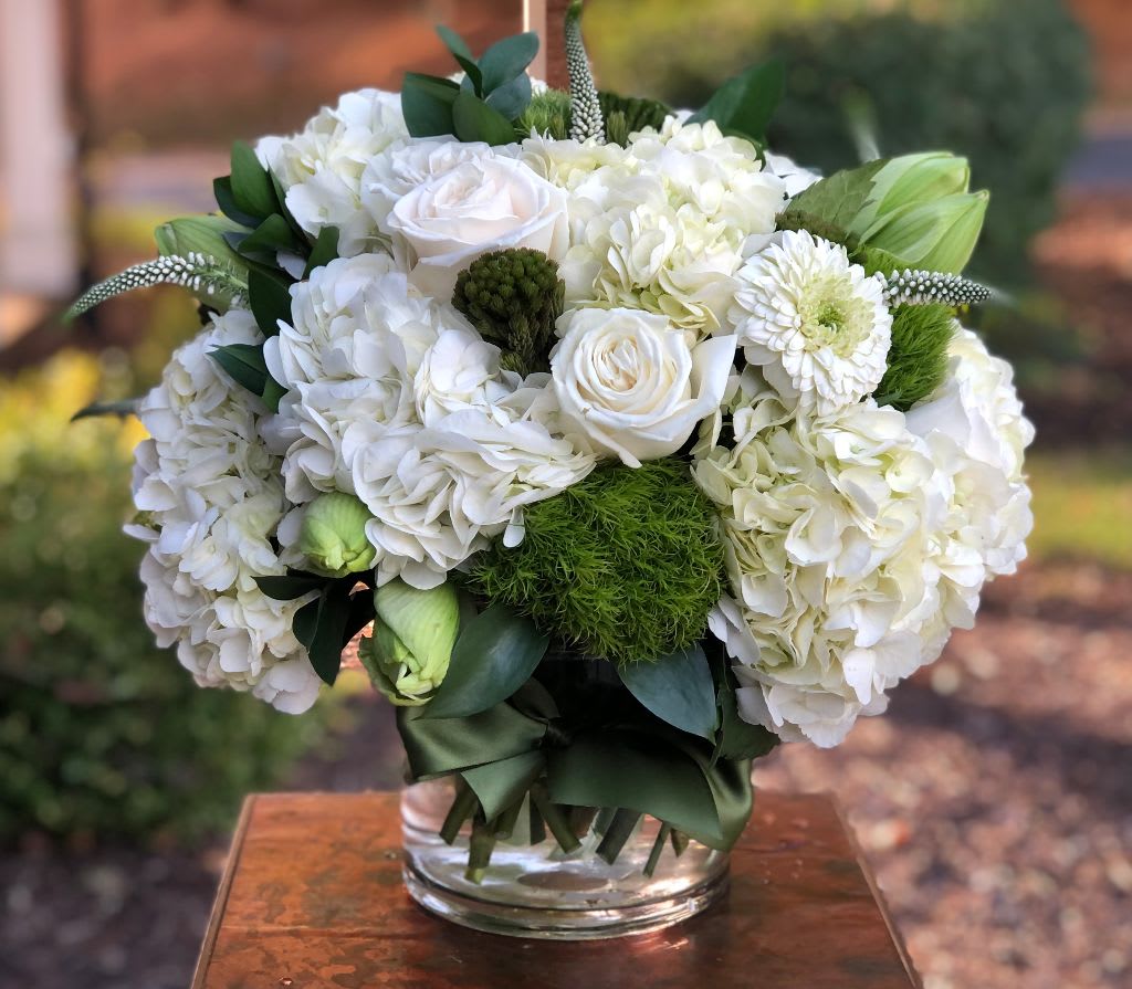 White floral arrangement in a clear glass vase with green accents