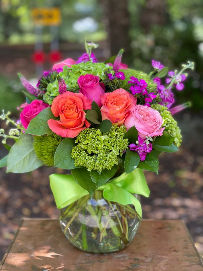 Pink and orange roses in a glass vase with green accents