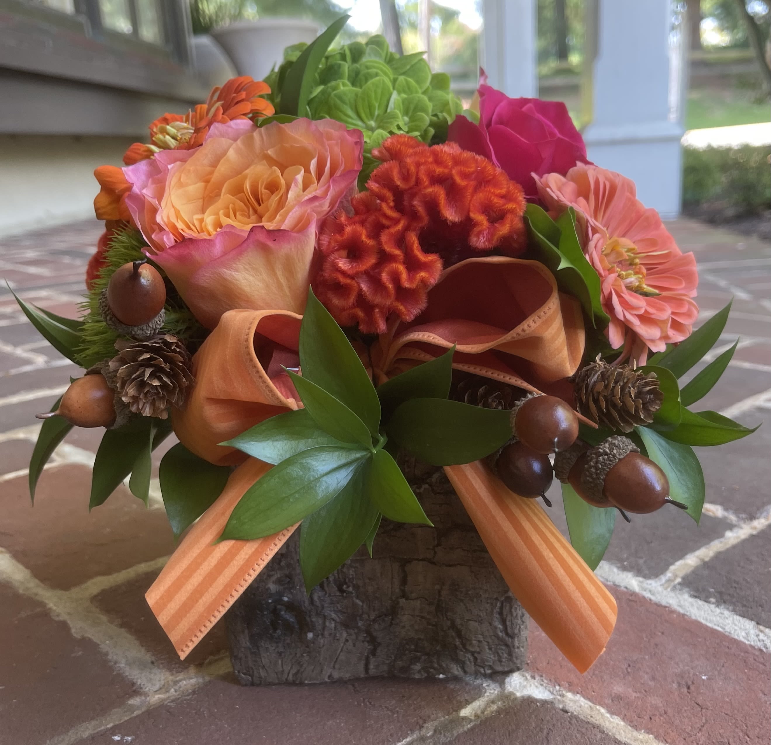 Orange and pink floral arrangement in a rustic wood container with ribbon