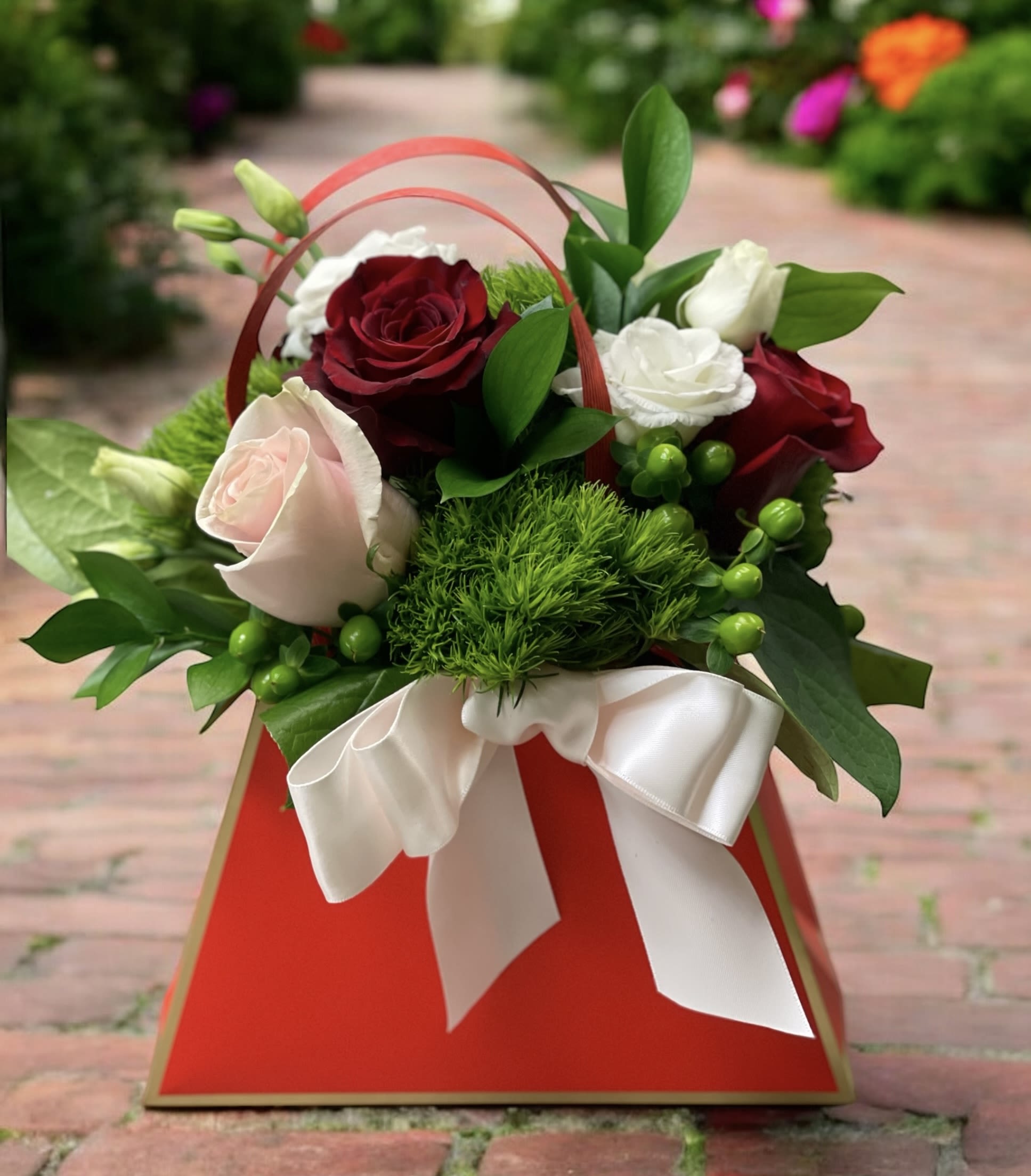 Pocket Full of Posies - Delight someone special with Pocket Full of Posies, a playful and romantic floral arrangement handcrafted by your trusted local florist in Wilmington, Delaware. This eye-catching design features lush greenery, rich dark red roses, soft pink roses, and elegant white lisianthus, all beautifully arranged in a fun red bag and finished with a coordinating satin ribbon. It’s a unique and cheerful twist on classic rose arrangements, perfect for making a memorable impression.  Ideal for birthdays, anniversaries, Valentine’s Day, or just-because surprises, Pocket Full of Posies brings color, joy, and heartfelt charm to any occasion.   At Petals Flowers and Fine Gifts, we specialize in creating custom, luxury floral designs with premium flowers and exceptional attention to detail. As a local florist in Wilmington, Delaware, we proudly offer same-day, tax-free flower delivery throughout Wilmington, Hockessin, Newark, Glen Mills, Chadds Ford, Kennett Square, and surrounding areas — all backed by our satisfaction guarantee.  Why Choose Us?  * Locally owned Wilmington florist known for creativity, quality, and personalized service * Hand-crafted floral arrangements tailored to every occasion * Reliable same-day delivery to homes, offices, and venues throughout the area Order Pocket Full of Posies today and let Petals Flowers and Fine Gifts deliver a beautiful expression of your sentiments right to their doorstep in Wilmington, Delaware.