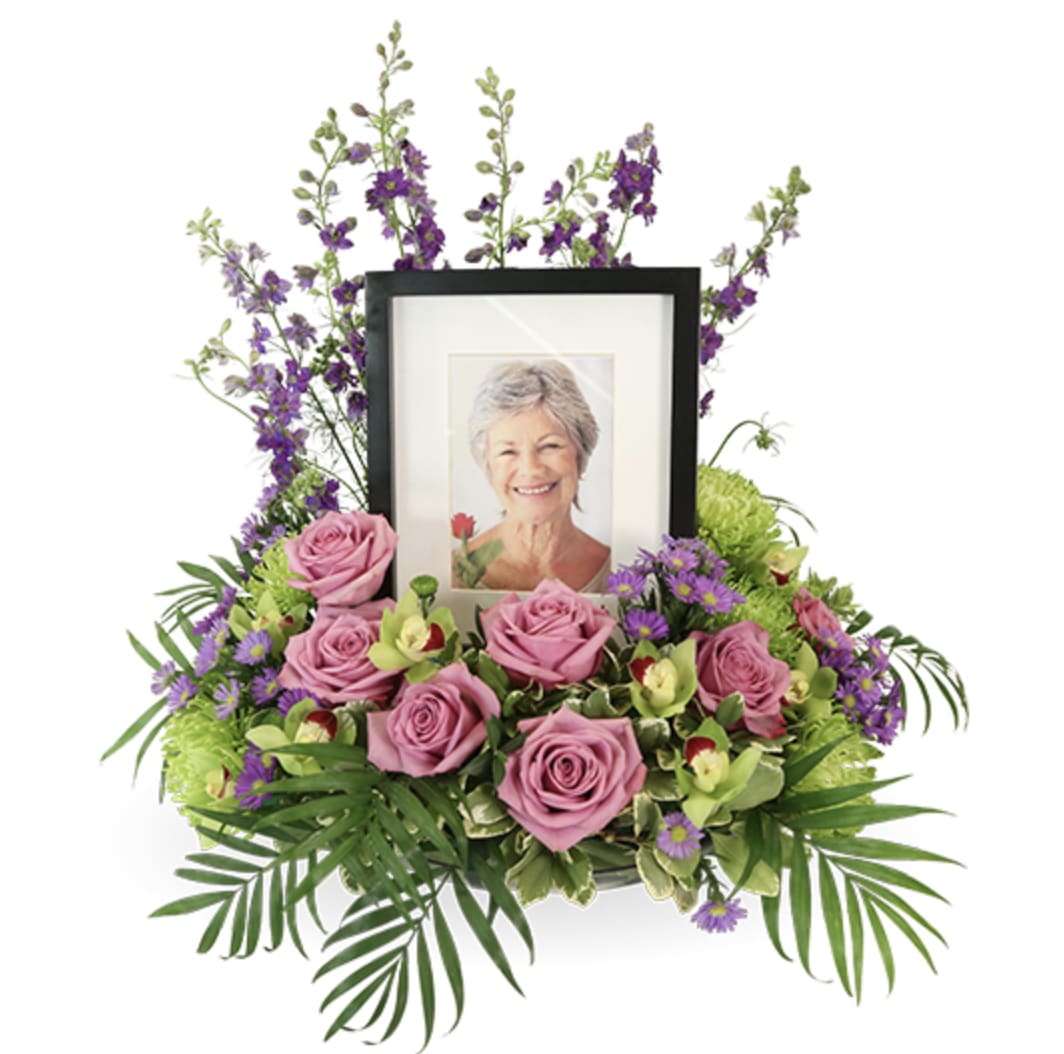 Eternal Peace Wreath - Eternal Peace Wreath | Wilmington, Delaware Florist  Celebrate a life of beauty and serenity with our Eternal Peace Photo Tribute, a graceful floral arrangement handcrafted by Petals Flowers and Fine Gifts in Wilmington, Delaware. This thoughtful design frames a cherished photo with soft pink roses, green cymbidium orchids, and vibrant purple larkspur, accented with fresh greenery. Wreath measures 12" in diameter.  Elegantly styled to honor a loved one during memorial or cremation services, Eternal Peace offers a peaceful and personal tribute that reflects cherished memories and the quiet strength of everlasting love.  As your trusted local florist in Wilmington, Delaware, we take pride in handcrafting every arrangement with premium blooms and genuine care. We offer same-day, tax-free delivery throughout Wilmington, Hockessin, Newark, Chadds Ford, Glen Mills, Kennett Square, and surrounding communities.  Why Choose Us?  * Custom, luxury floral designs with a satisfaction guarantee * Locally owned flower shop in North Wilmington, Delaware * Friendly, personal service with delivery to your loved ones’ doorsteps Send the Eternal Peace Photo Tribute to honor a life well loved throughout Wilmington and surrounding areas.