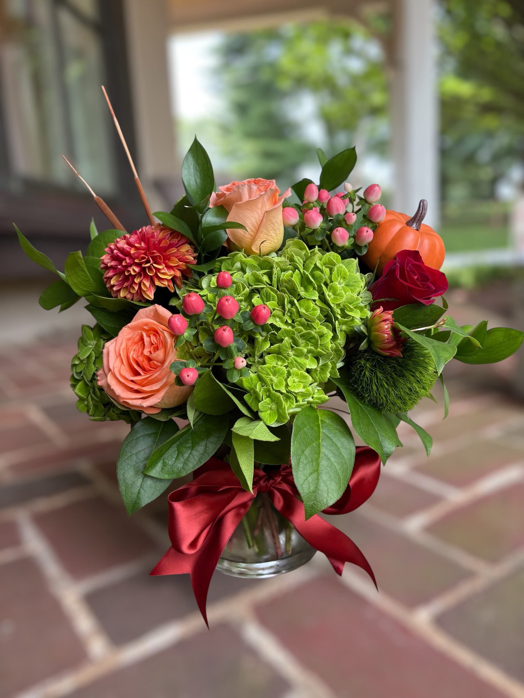 Cinnamon Spice - Cinnamon Spice | Wilmington, Delaware Florist Celebrate the warmth of the season with Cinnamon Spice, a stunning fall floral arrangement handcrafted by Petals Flowers and Fine Gifts in Wilmington, Delaware. This festive design features lush green hydrangea, peach hypericum berries, soft peach roses, and classic red roses, accented with rustic cattails and charming faux pumpkins for a touch of autumn harvest flair. Styled in a modern glass cylinder vase, Cinnamon Spice brings together rich seasonal colors and textures in an elegant, inviting display. Perfect for Thanksgiving centerpieces, autumn celebrations, birthdays, or simply sending cozy seasonal cheer, Cinnamon Spice is a versatile arrangement that adds a touch of fall elegance to any home, office, or gathering. Its balance of fresh blooms and festive accents makes it a memorable gift or a standout décor piece. As your trusted local florist in Wilmington, Delaware, Petals Flowers and Fine Gifts creates luxury floral designs with premium flowers and seasonal details. We are proud to offer same-day, tax-free flower delivery throughout Wilmington, Hockessin, Newark, Chadds Ford, Glen Mills, Kennett Square, and surrounding communities, ensuring your gift arrives fresh and beautiful. 