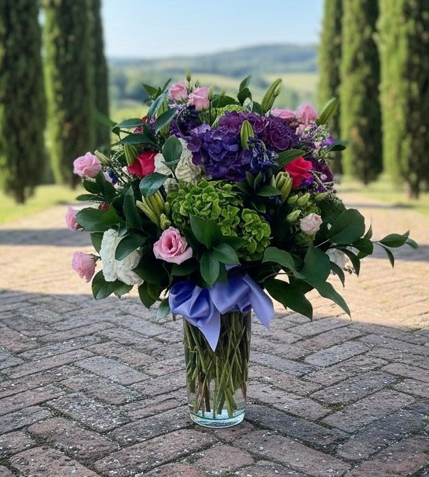 Bouquet of pink and purple flowers in a clear glass vase with a lavender ribbon