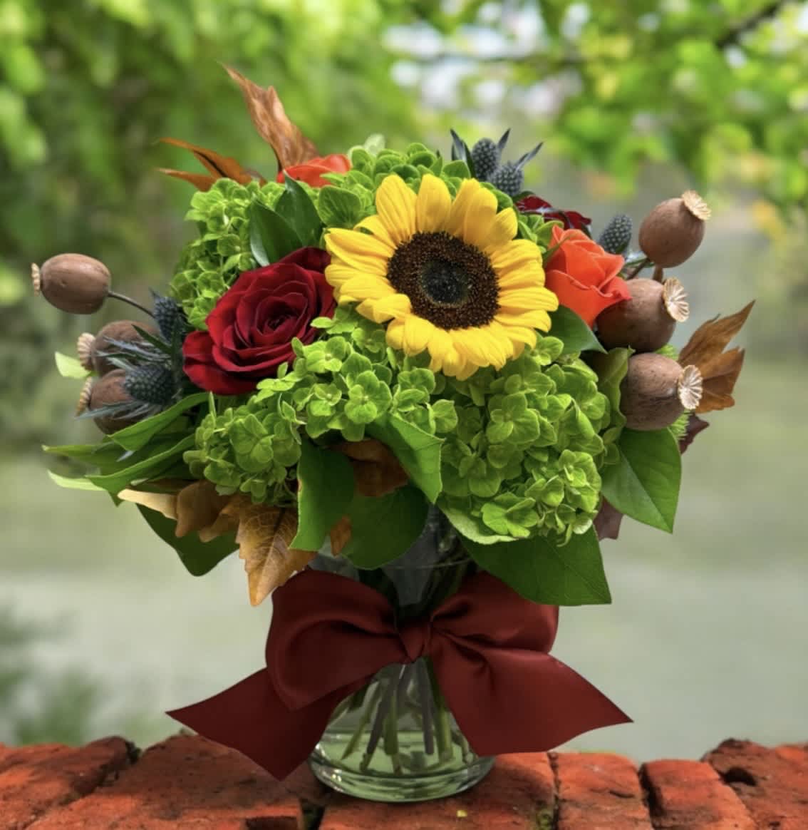 Bouquet with a sunflower, red and orange roses, and green hydrangeas in a glass vase