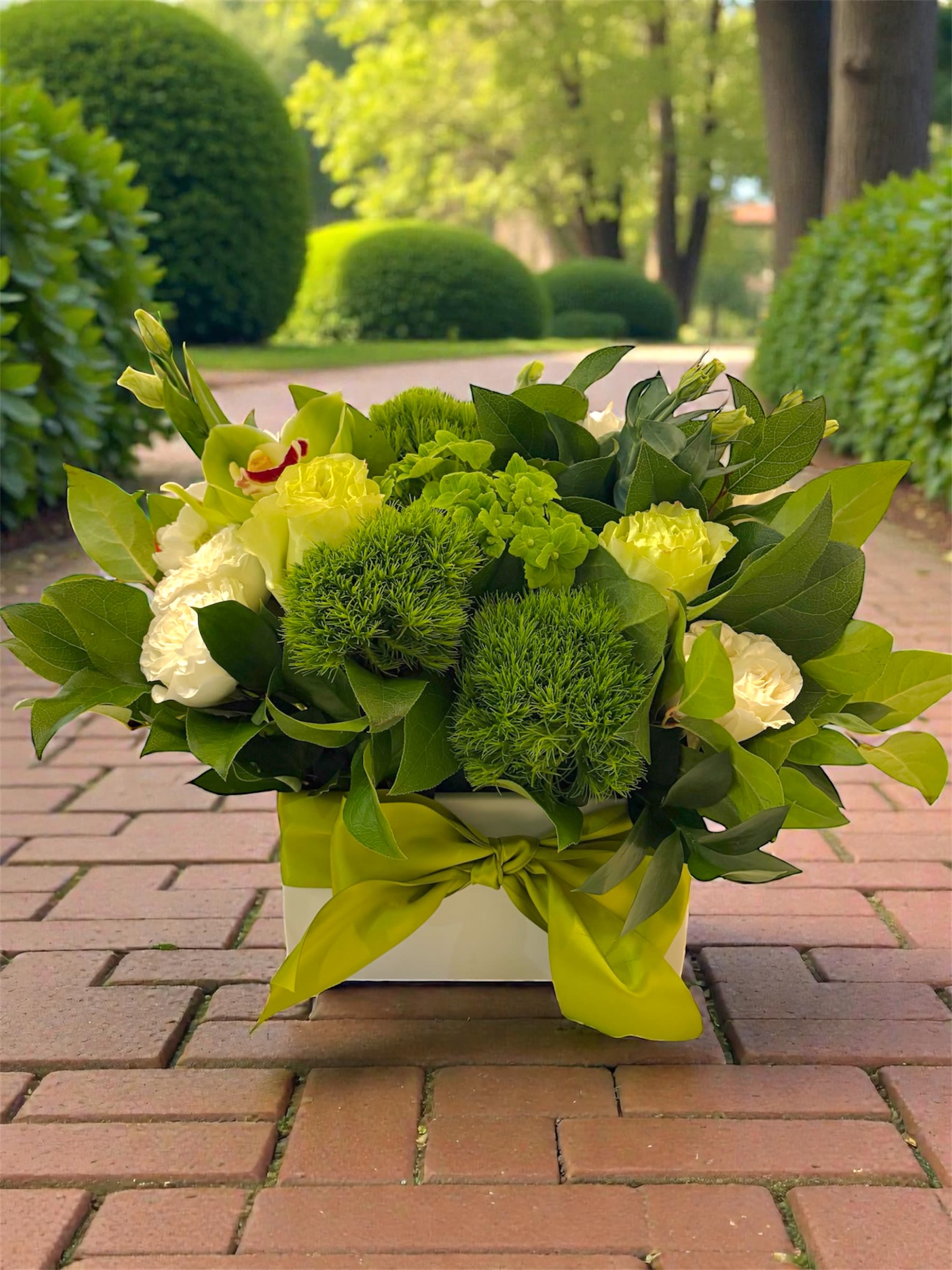Green and white floral arrangement in a square box with a ribbon