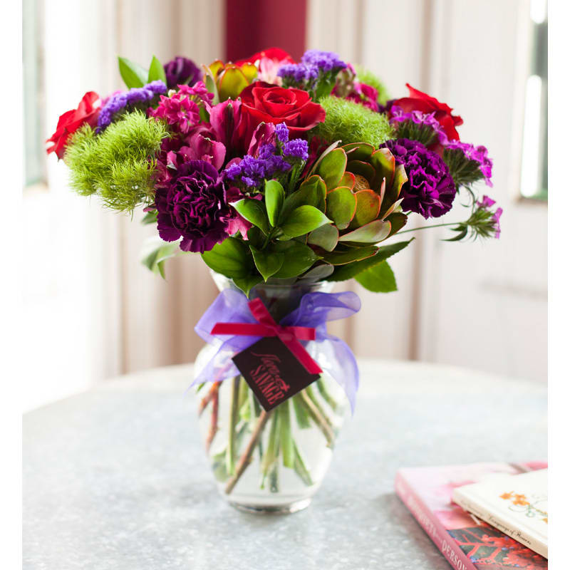 Bouquet of red, purple, and pink flowers in a glass vase with a ribbon