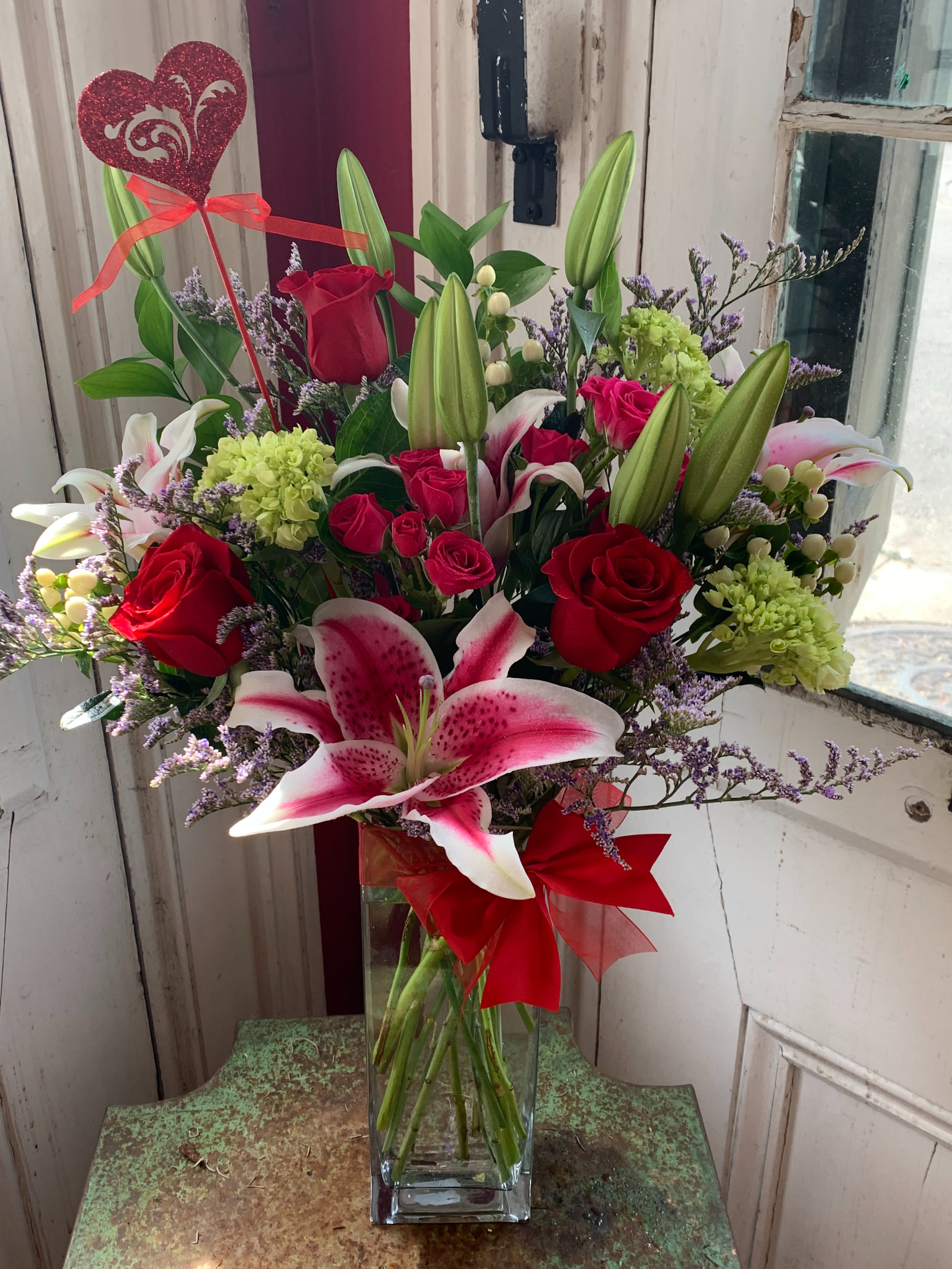 Bouquet of red roses and pink lilies in a glass vase with a heart pick