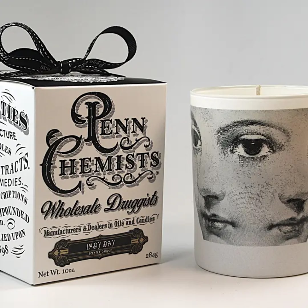 A boxed candle with a black ribbon sits beside a printed candle jar.