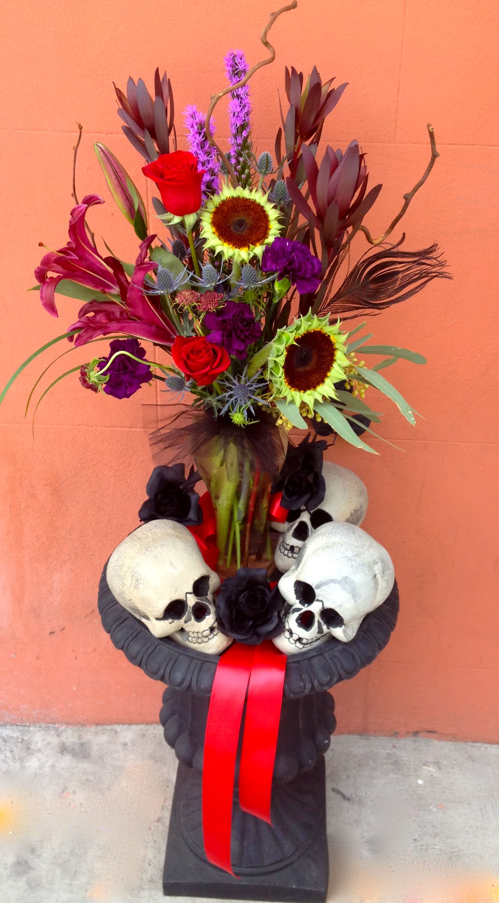 Tall floral arrangement with sunflowers, red roses, lilies, and skull decorations