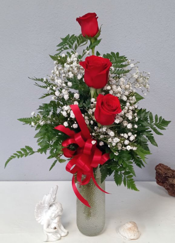 Three red roses in a glass vase with baby's breath and a red ribbon