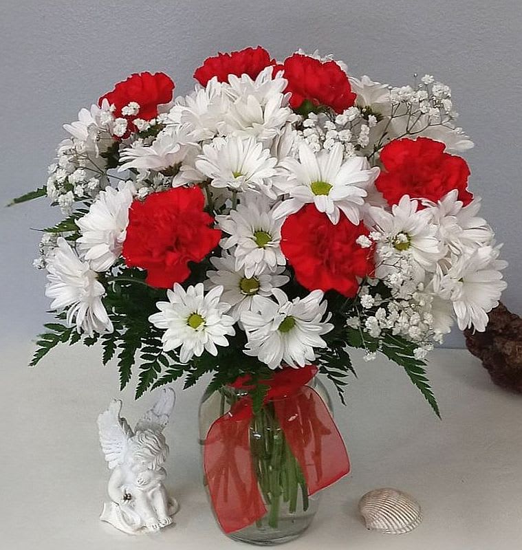 Red carnations and white daisies in a glass vase with a red ribbon
