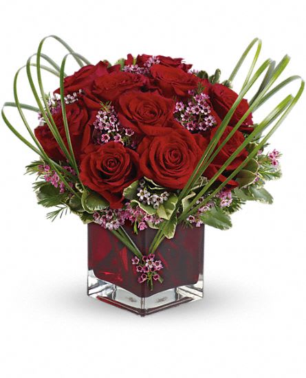 Red roses arranged in a square glass vase with looping grass accents