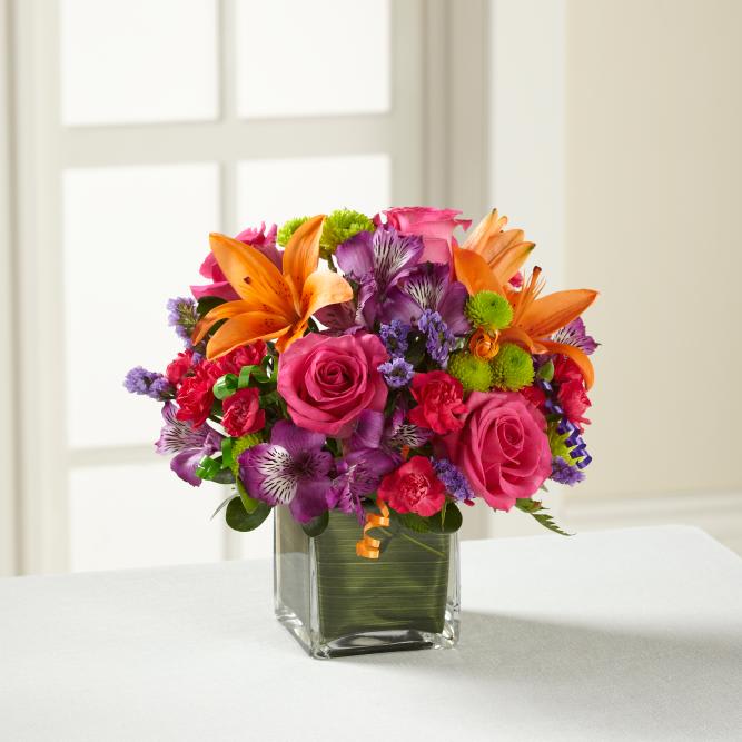 Colorful bouquet of roses, lilies, and purple flowers in a glass vase