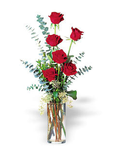 Tall arrangement of red roses in a clear glass cylinder vase with accent foliage