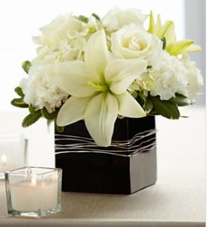 White lily and rose arrangement in a black square box with a candle nearby