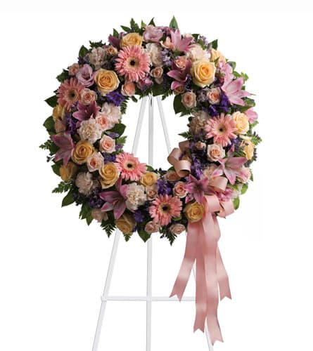 Pastel floral wreath on a white stand with a pink ribbon
