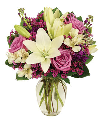 Bouquet of pink roses, white lilies, and purple filler in a glass vase
