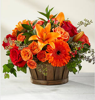 Orange and red mixed flower arrangement in a wooden basket