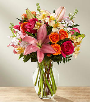 Mixed bouquet of pink lilies, roses, and orange blooms in a glass vase