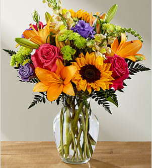Colorful bouquet of lilies, roses, and a sunflower in a clear glass vase