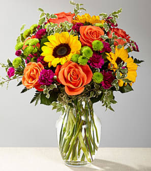 Bouquet of orange roses, sunflowers, and magenta mums in a glass vase