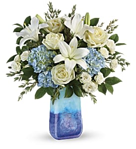 White lilies, roses, and blue hydrangeas in a blue glass vase