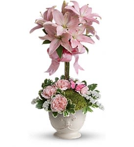 Tall pink lily topiary with pink carnations and white filler flowers in a white ceramic urn.
